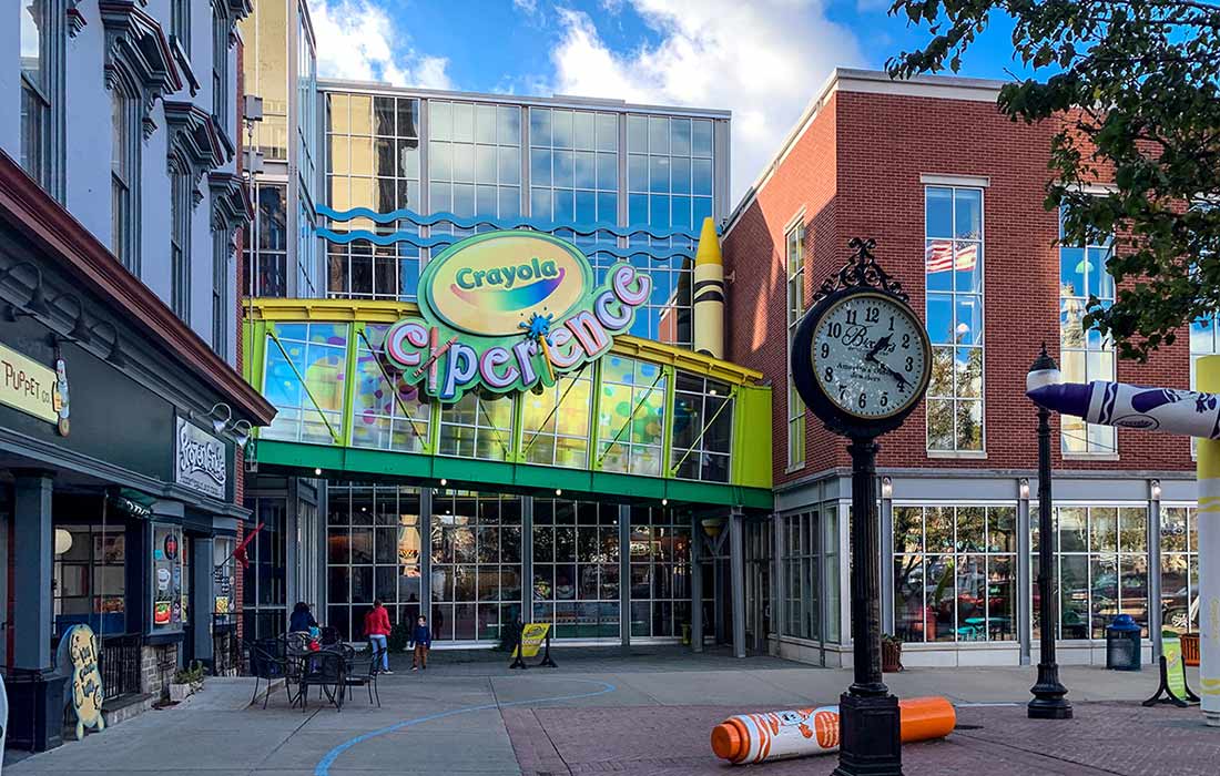 Crayola Experience entrance in Easton, Pennsylvania, featuring colorful signage, giant crayon decorations, and nearby outdoor seating.